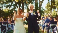 Wedding videography still of bride and groom walking down aisle with guests seated on both sides