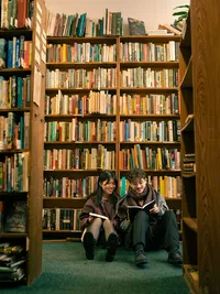 A couple sits with their back against a bookshelf in a library, by Grand Rapids couples photographer Grace Wan.