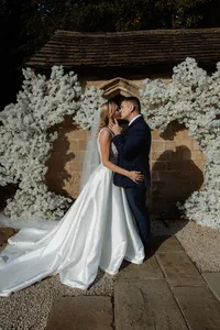 couple kissing outside wedding venue with white floral display around the entrance