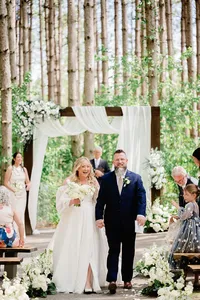 Bride and groom holding hands at the end of a wedding ceremony in the forest.