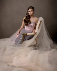 Teen girl in a flowing tulle gown seated on an antique chair during her studio portrait session