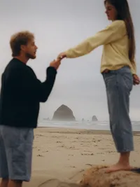 Grand Rapids couples photographer Grace Wan captures a man holding his fiancé's hand, behind them Haystack Rock.