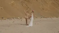 bride in white gown with groom in tan suit on beach - Wedding videography still of bride and groom standing together on expansive sandy beach with groom in tan suit