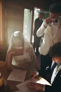 bride and groom veil preparation moment - Photograph of bride adjusting her veil with groom assisting during indoor preparing moment with warm window light