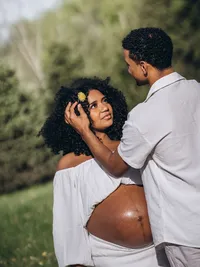 A man tucks a flower behind his pregnant wife's ear, by Grace Wan Michigan maternity photographer.