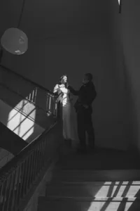 Black and white photo of Grace and Jacob standing on a marble staircase in dramatic window light, by Dove and Fox