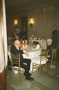 Photograph of two guests dining at small white-clothed table in elegant formal room with warm ambient lighting