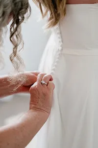Mother of the bride helping a bride do up her buttons on her wedding dress while taking photos.