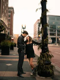 A woman holds onto a streetlamp as she smiles at her fiancé during their Grand Rapids engagement photography session.