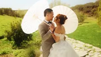 Wedding videography still of couple holding decorative white umbrella in outdoor garden setting