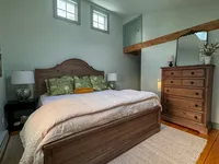 Primary bedroom with exposed wood beams and antique-style furnishings at Brookside Retreat