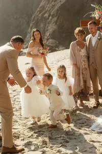 family group on sandy beach - Photograph of bride with family members and flower girls in white dresses gathered together on sandy beach area