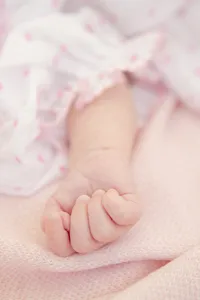 Close-up of newborn baby's hand grasping against a pink blanket