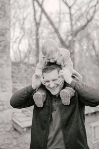 Father carrying his child on his shoulders along a wooded path