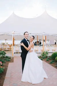 Bride and groom pose together in front of a white reception tent
