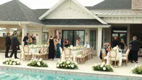 Wedding videography still of white tent or pavilion reception setup with seated guests and white floral arrangements