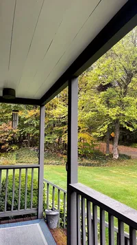Wood-burning fire pit with flames and stacked firewood at Brookside Retreat
Covered front porch overlooking autumn foliage at Brookside Retreat