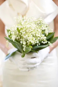 Close-up of a lily of the valley bouquet held in white gloved hands