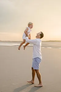 Father lifting his toddler in the air during a sunset beach portrait session