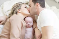 Parents sharing a kiss over their newborn baby
