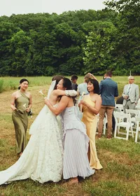 bride embraced by guests in field - Photograph of bride surrounded by guests in earth-tone attire celebrating together in open grassy field