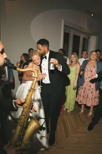 groom dancing with guest and saxophonist - Photograph of groom in formal tuxedo dancing with female guest while saxophonist performs with gold saxophone nearby