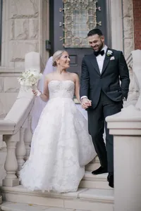 Bride and groom smile walking down stone steps outside an arched wooden door