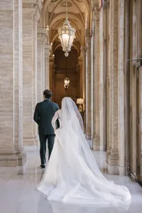 Bride and groom walk together down an ornate marble hallway beneath a painted vaulted ceiling