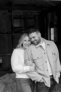 Couple embracing on a hay bale during their engagement session, photographed in black and white