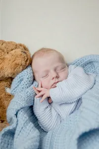 Newborn baby wrapped in a blue blanket beside a teddy bear
