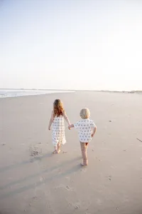 Siblings walking hand in hand toward the ocean