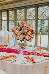 bright floral wedding table centrepiece with a pink table runner and orange napkins
