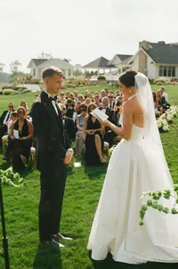 bride and groom exchanging vows at ceremony - Photograph of bride and groom facing each other during outdoor ceremony with seated guests visible around them on lawn
