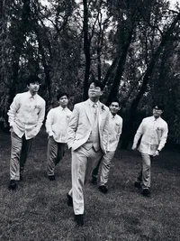Black and white portrait of a groom walking with all his groomsmen behind him.
