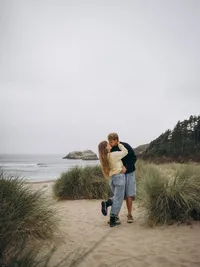 A man holds his fiancé around the waist as they go in for a kiss on Cannon Beach, Oregon.