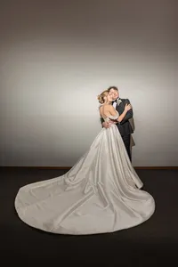 Bride and groom embracing in a studio with her long satin train spread across the floor