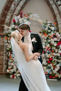 couple kissing in front of colourful wedding floral arch