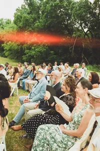 outdoor reception with bonfire - Photograph of guests seated outdoors during reception with glowing bonfire or fire pit visible in background against tree line