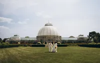 A bride and groom walk towards the camera with the Belle Isle Conservatory behind them.