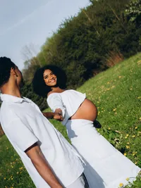 A husband and wife hold hands as they smile at each other, by Grand Rapids maternity photographer Grace Wan.