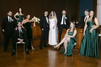 Grace and Jacob posing with their wedding party in green dresses and black tuxedos in a wood-panelled hall, by Dove and Fox