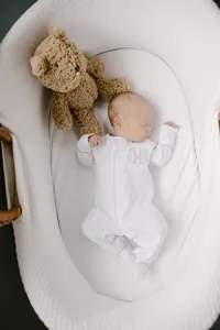 Newborn baby in a lounger wearing a monogrammed outfit beside a teddy bear