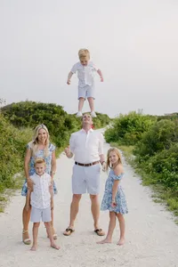 Family portrait on a beach pathway with child jumping mid-air