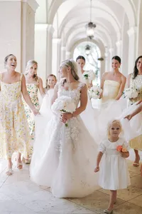 Bride walks through an arched courtyard with bridesmaids in yellow floral dresses
