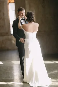 Grace holding Jacob's face as they smile at each other in a sunlit hall on their wedding day, by Dove and Fox