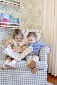 Siblings reading together in a gingham chair
