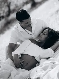 Black and white maternity portrait of a pregnant mother lying on her husband's lap.