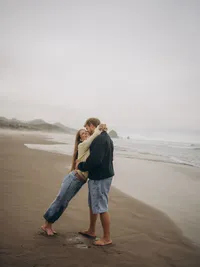 A woman leans against her fiancé during their engagement photos on Cannon Beach, Oregon.