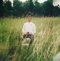 groom standing in tall grass field - Photograph of groom in white dress shirt posed alone in open grassy field with soft natural lighting on film