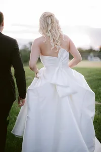 Bride's oversized bow dress detail seen from behind as she walks beside the groom